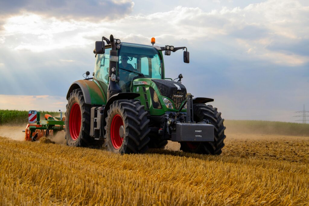 pexels-photo-2933243-2933243 A powerful green tractor plowing a dusty wheat field under a cloudy summer sky in rural Germany.